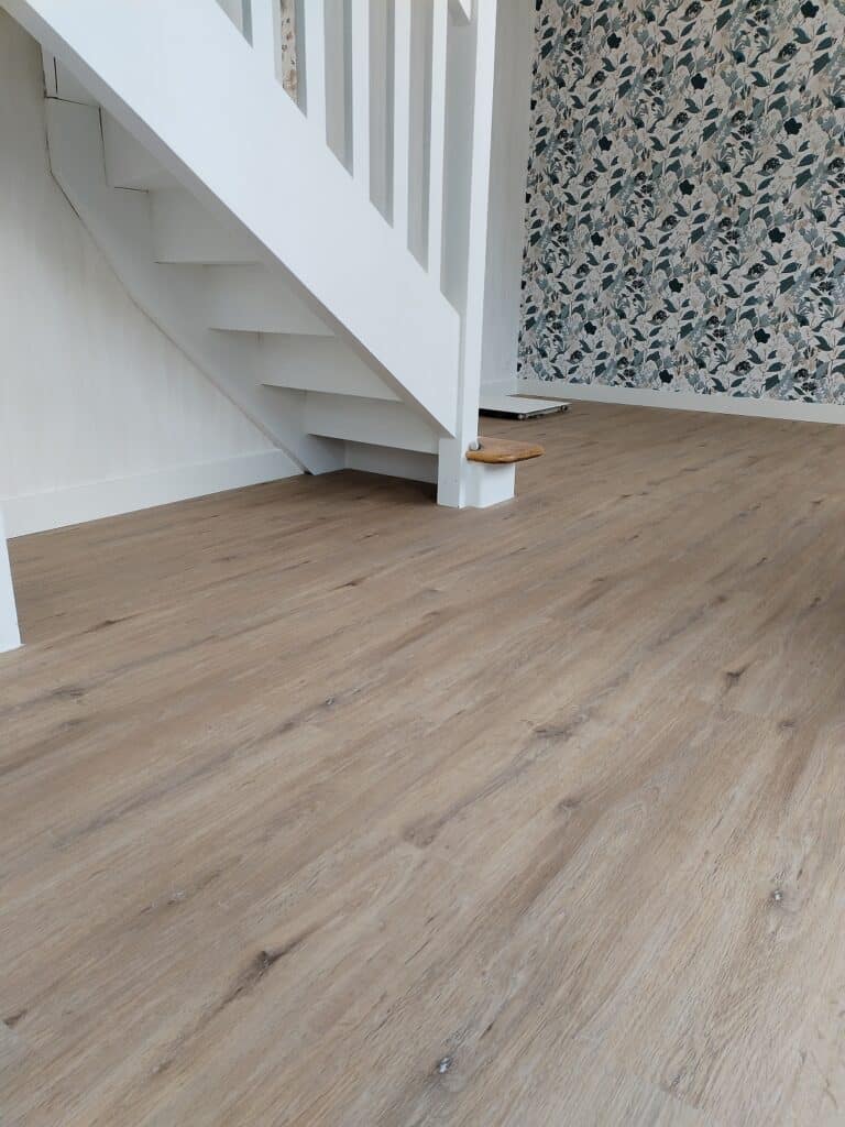 Escalier blanc moderne avec rampe, sol en bois clair et papier peint floral vert dans une pièce lumineuse.