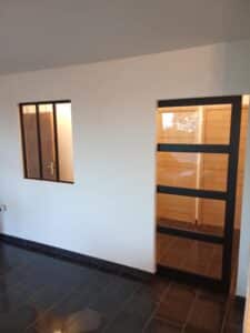 Intérieur moderne avec murs blancs, carrelage noir brillant et une fenêtre ainsi qu'une porte vitrée noire minimaliste.